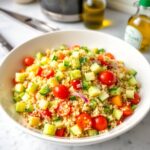 A vibrant gluten free quinoa salad in a bowl, featuring diced cucumber, bell pepper, red onion, halved cherry tomatoes, and fluffy quinoa, drizzled with a light lemon dressing. The scene is radiant and luxurious, with an ad